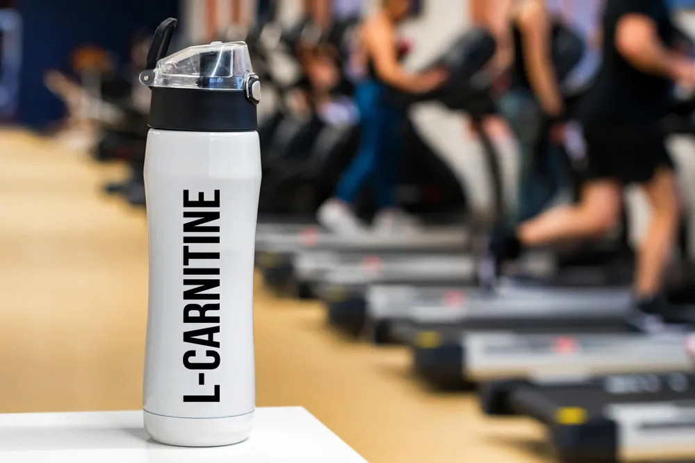 A picture of a sports bottle of L-Carnitine in a gym, there are people in the background working out.